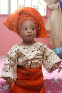 Baby girl in cream buba aso-oke, with orange iro and gele.